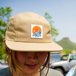 Khaki five panel hat with retro orange and navy mountain logo worn by model outside